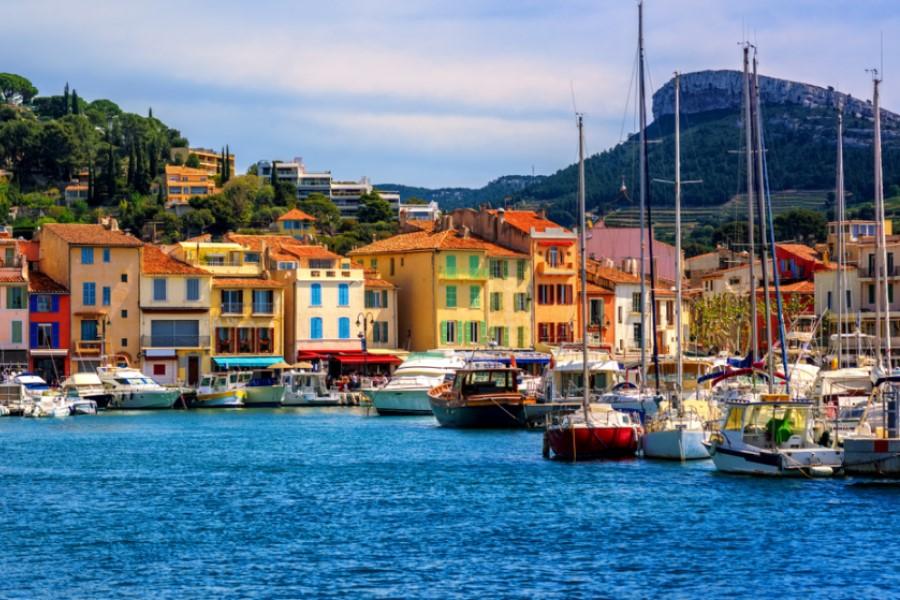 Colorful houses with red roofs at the harbor before wooded hills. Numerous boats and yachts are in the water. Popular cruise routes often lead to such picturesque coastal towns.