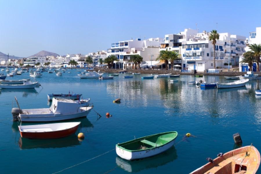 Small boats float on blue water in a harbor; in the background, white buildings and palm trees. Popular cruise routes lead to such picturesque places with typical coastal towns.