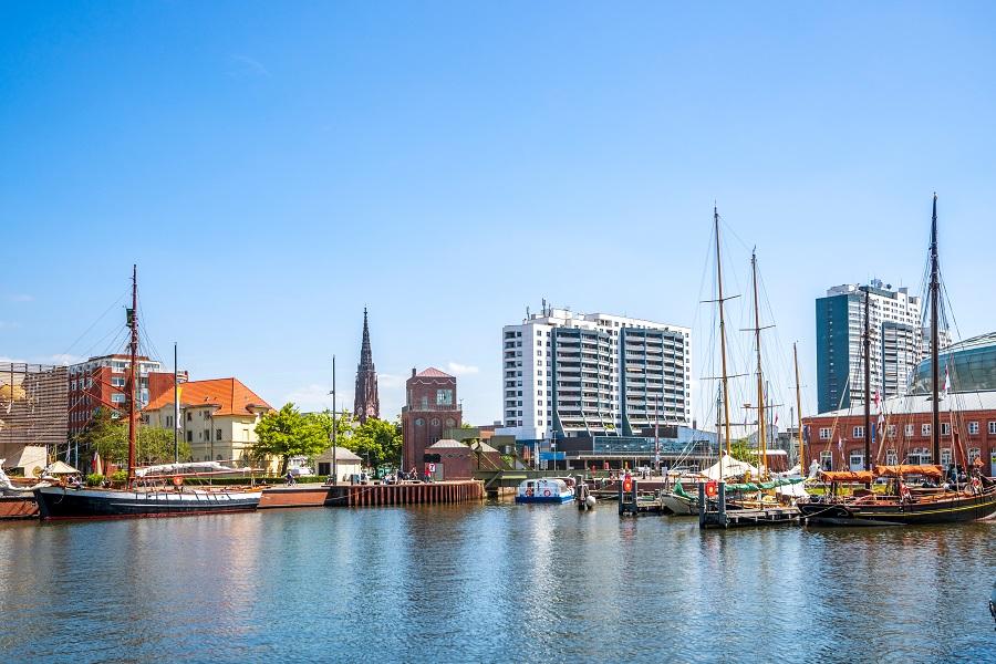 Several sailing ships are moored at the harbor in Bremerhaven. In the background, modern buildings and a church tower rise. This city is one of the most popular cruise destinations in Northern Europe.