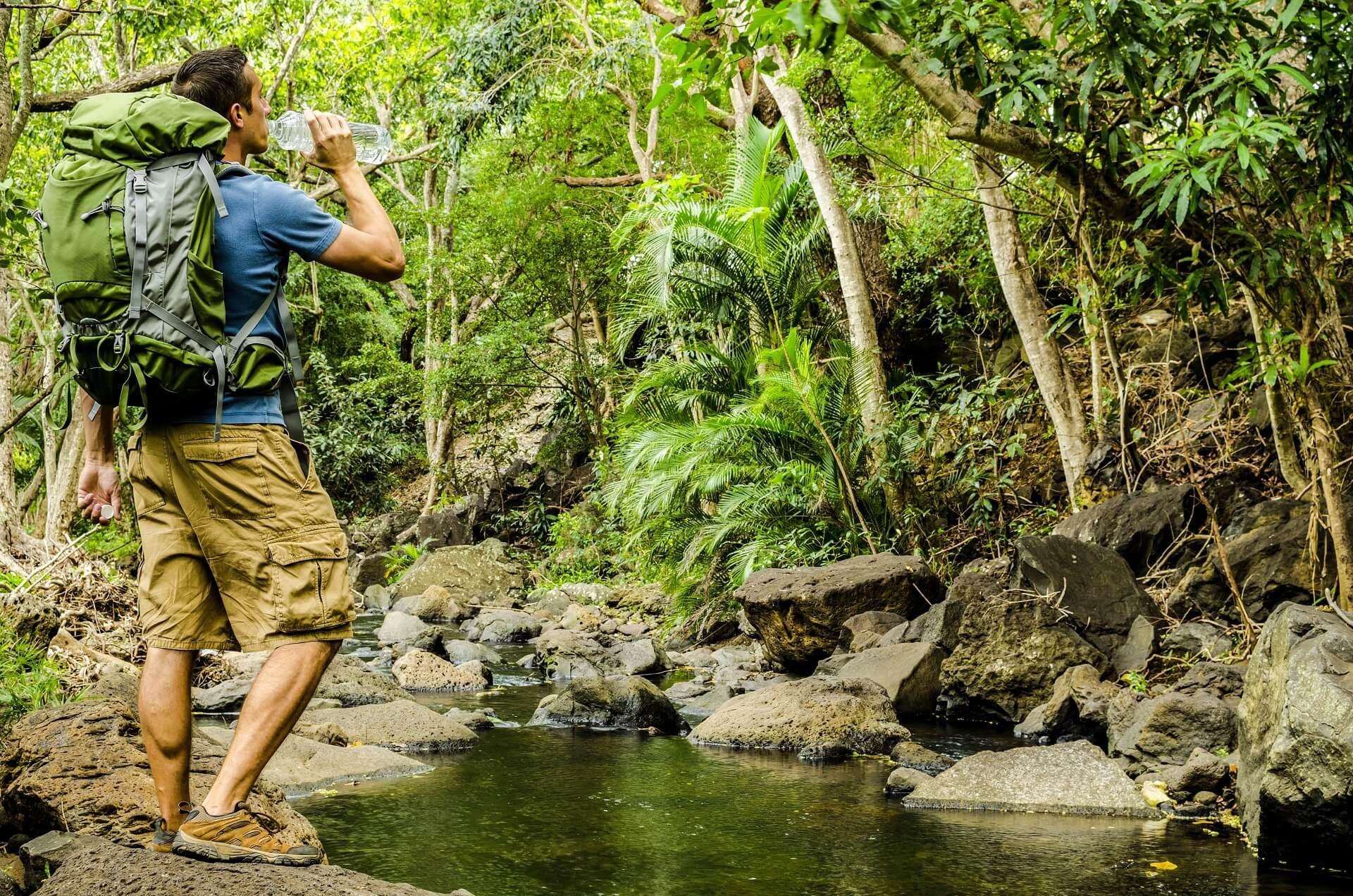 Hiker drinks water in the jungle by a stream