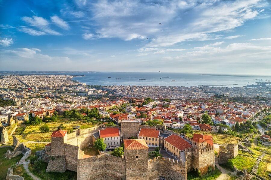 Panorama of Thessaloniki with ancient fortress walls in the foreground and the Aegean Sea on the horizon under a clear blue sky.