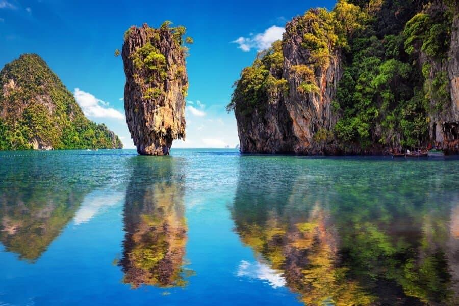 Limestone cliffs rise impressively from the turquoise water. Right is dense green jungle, left a single rock. The clear reflection enhances the tropical idyll.