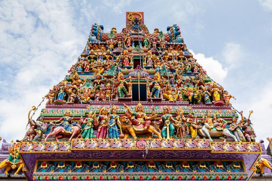 Colorful, richly decorated Hindu temple with numerous, intricately detailed deity figures. The figures are arranged in several tiers, extending to the top of the tower.