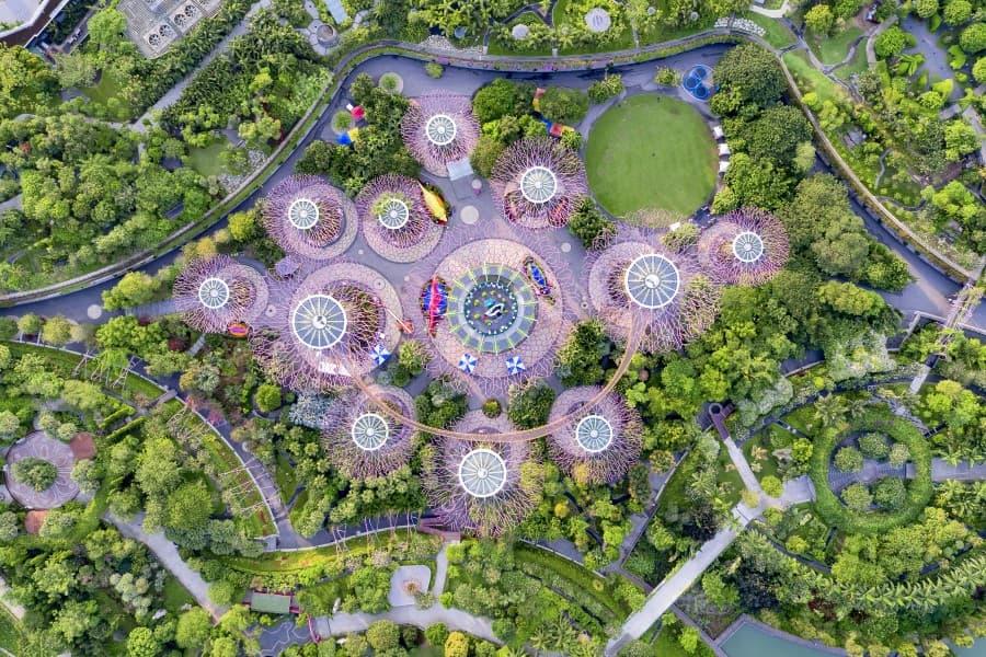 Aerial view of Singapore's Gardens by the Bay: Several round, tree-like structures set amidst lush greenery. A path winds through the area, surrounded by dense vegetation.