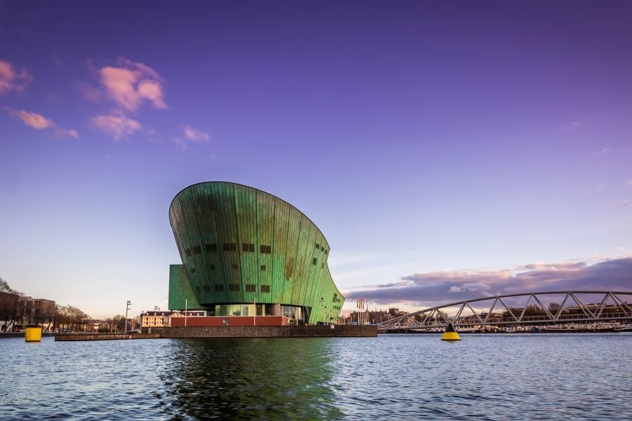 The green, ship-like NEMO Science Museum juts out over the water in Amsterdam against a blue sky.