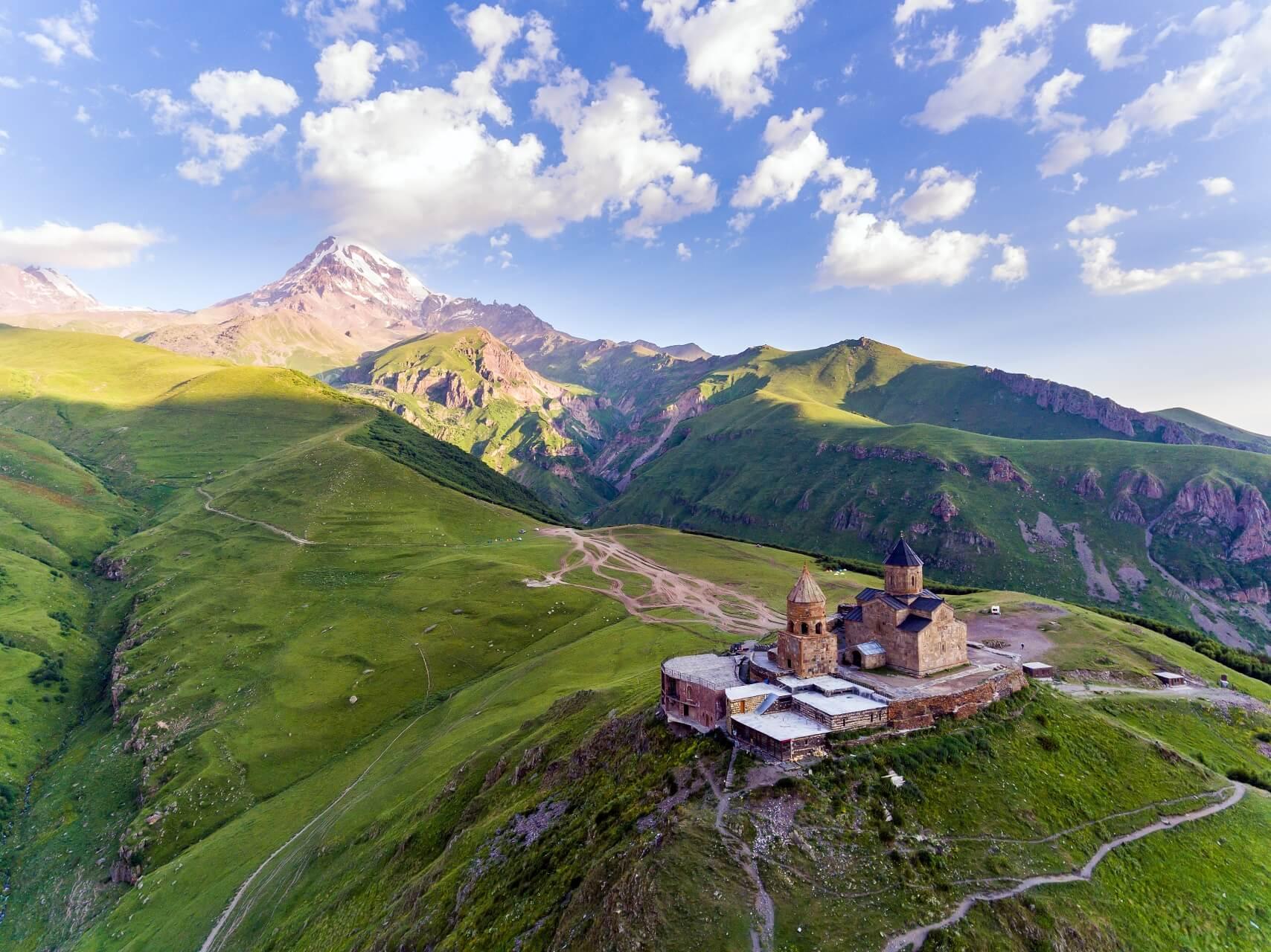 The Gergeti Trinity Church in Georgia from a bird's-eye view. The church stands lonely in the middle of green meadows on the mountain.