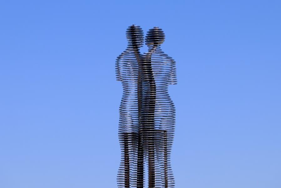 The figures Ali and Nino, made of steel, are merging together against a blue sky.