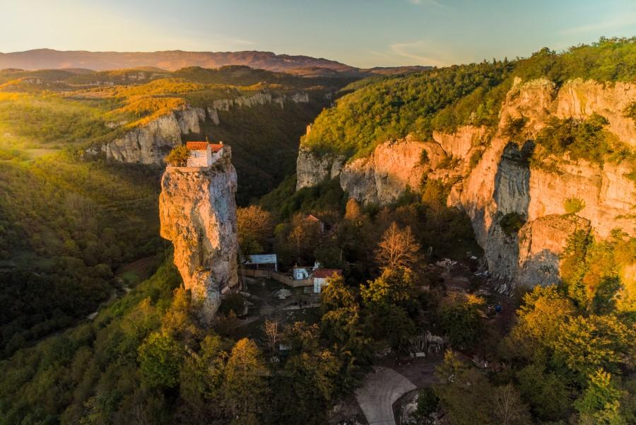 Aerial view of Katskhi Pillar. The sun is shining on the landscape, enveloping the green surroundings in a peaceful light. A church is recognizable on the high rock.