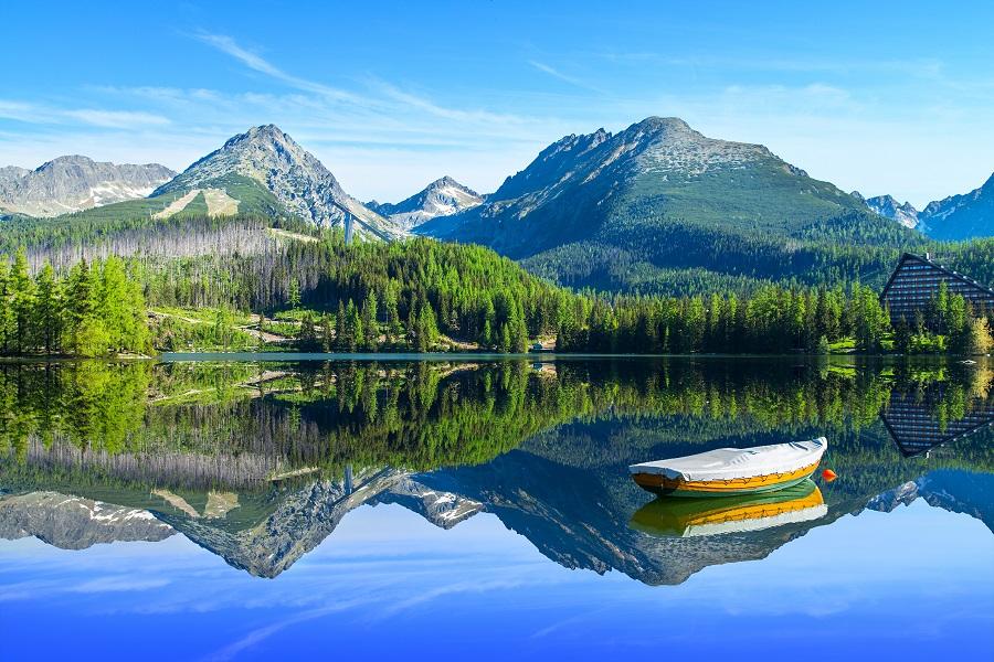 A lake in the High Tatras in Slovakia. A canoe floats on the lake, with mountains and forest reflected in the background.