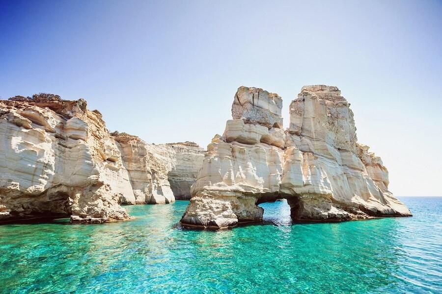 Limestone formations rise from the turquoise water of Kleftiko Bay, Milos. The sky is clear and blue, while the cliffs majestically dominate the right side of the image.