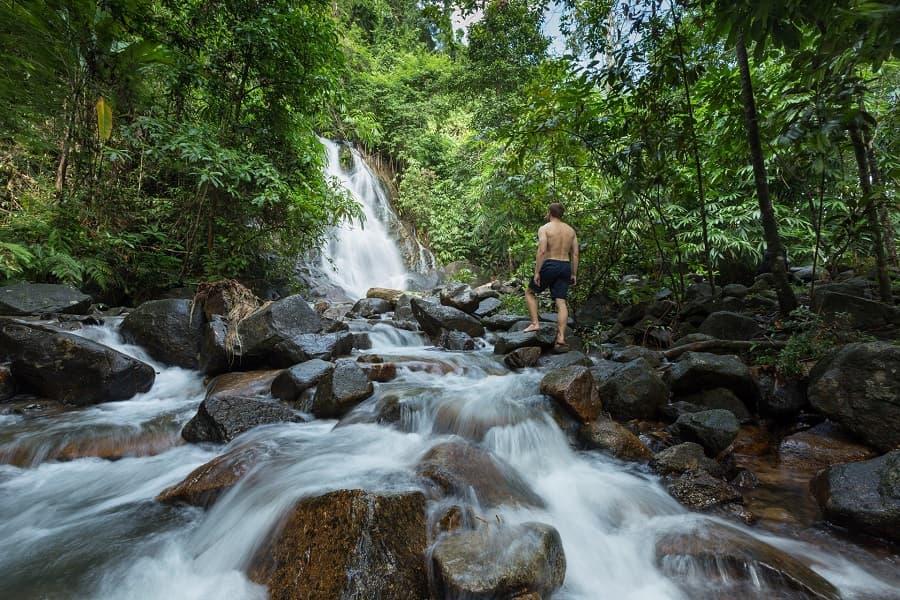 A man stands in front of a waterfall in the jungle near Khao Lak