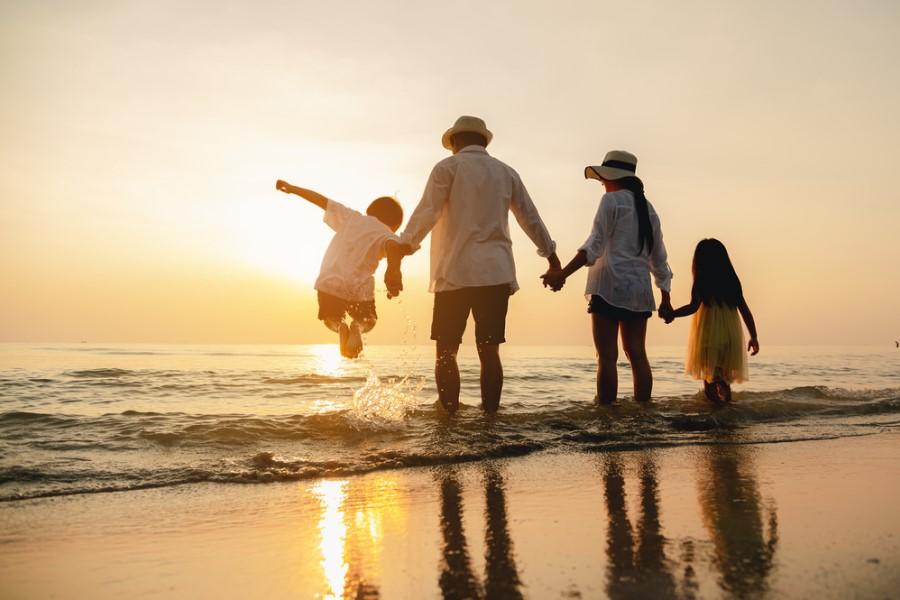 A family of four stands on the beach in the gentle waves, looking at the sunset.