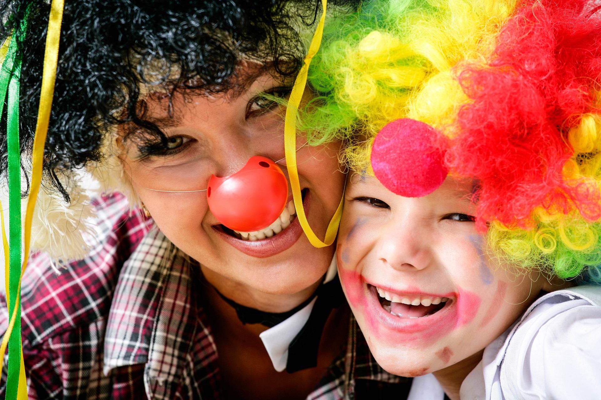 A costumed mother and her costumed child laugh at Carnival into the camera.