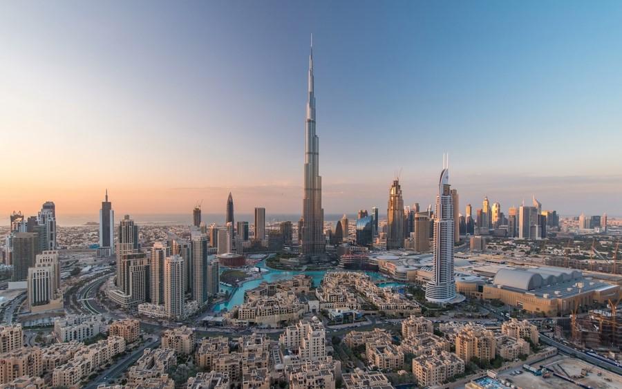 View of Dubai's skyscrapers at sunset with the Burj Khalifa at the center, surrounded by other tall buildings and water features. Perfect for a November cruise to explore modern architecture.