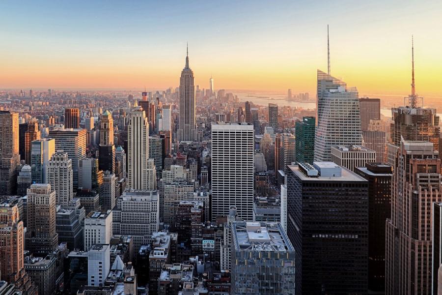 Skyscrapers of Manhattan at sunset. The sky glows orange and blue. Centrally, a distinctive building rises against the background of the Hudson River. Buildings are positioned in the middle and on the right.
