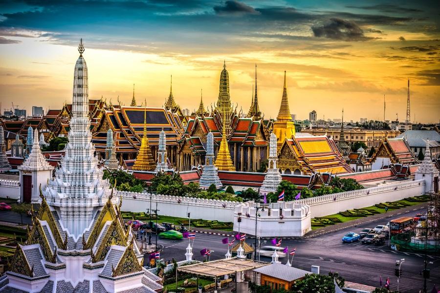 Sunset over the Grand Palace and Wat Phra Kaew in Bangkok, Thailand; magnificent golden and colorful roofs stand out against the colorful sky surrounded by white walls.