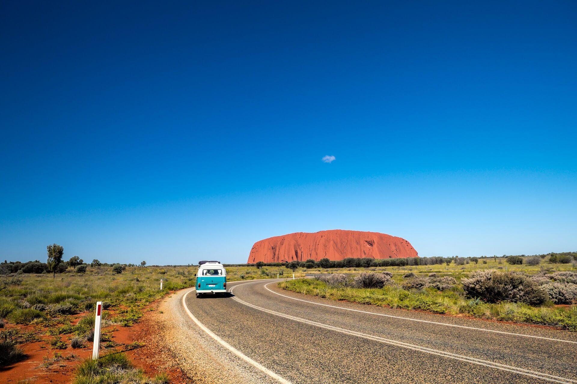 A van driving on a road trip through the Outback towards Ayers Rock.