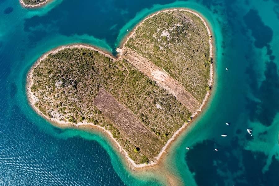 From a bird's eye view, the heart shape of the island Galesnjak in Croatia is immediately recognizable. Surrounded by turquoise water, the island itself is covered with many green trees.