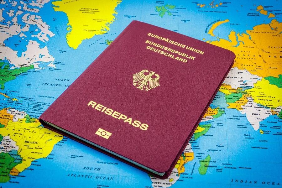 A German passport is tilted on a colorful world map. The passport is burgundy with golden lettering and crest, covering parts of Europe and Africa.