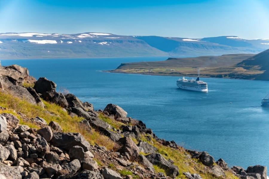 Photo of a cruise ship sailing through an Icelandic fjord, passing expansive fields towards tall mountains.