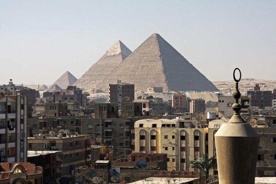 In the foreground, multi-story buildings with flat roofs on the outskirts of Cairo, behind them the pyramids.