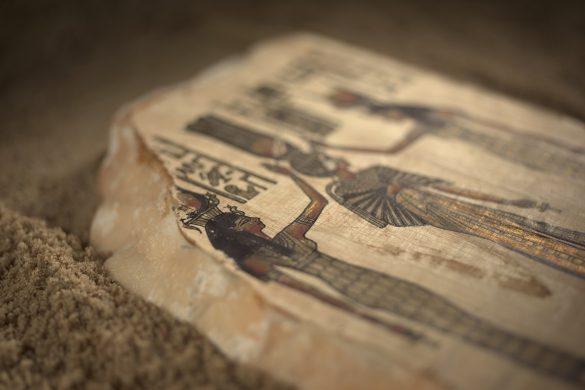 Egyptian paintings and hieroglyphs on a stone surrounded by sand.