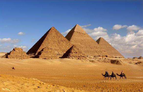 The three large and the smaller pyramids of Giza in the desert, with some camels in the foreground.