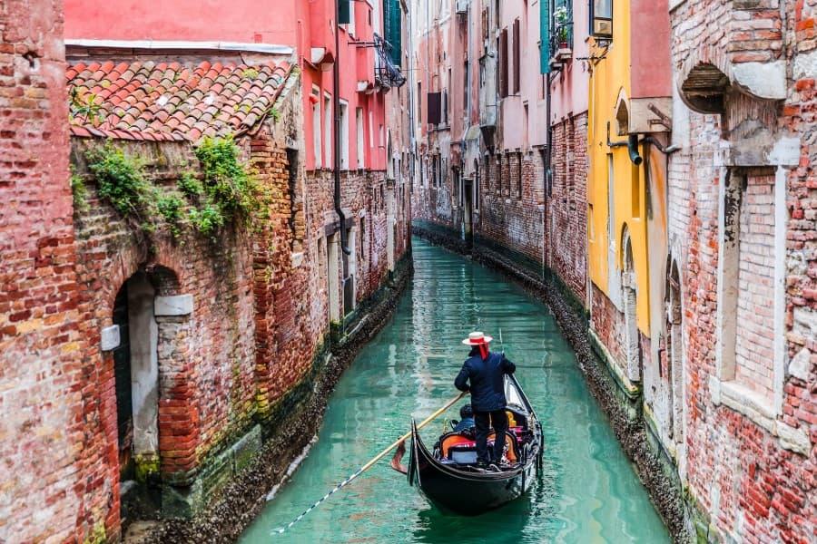 venetian-gondolier-punting-gondola-through-green-canal-waters-of-venice