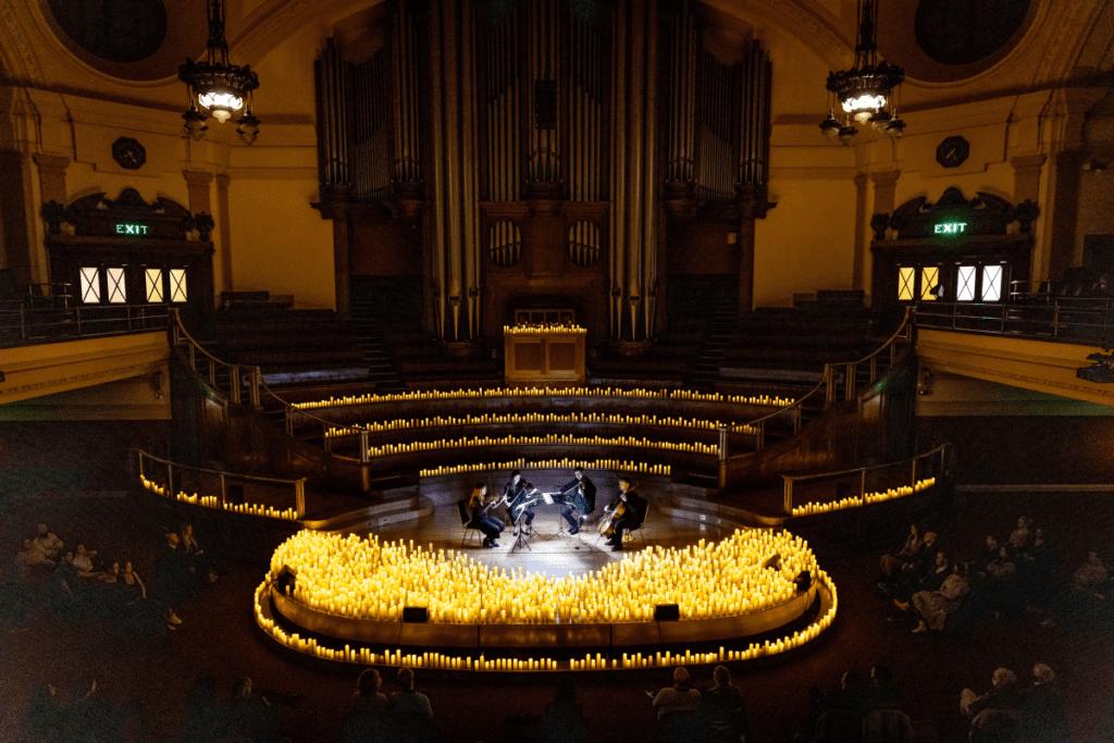 A string quartet performing on stage surrounded by candlelight in Central Hall Westminster.